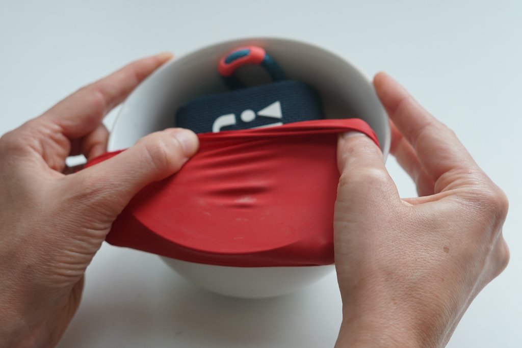 Zwei Hände spannen einen roten Ballon über eine Schüssel mit Lautsprecher