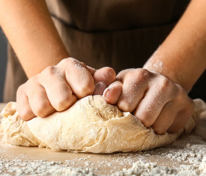Les mains pétrissent la pâte levée sur le plateau de la table