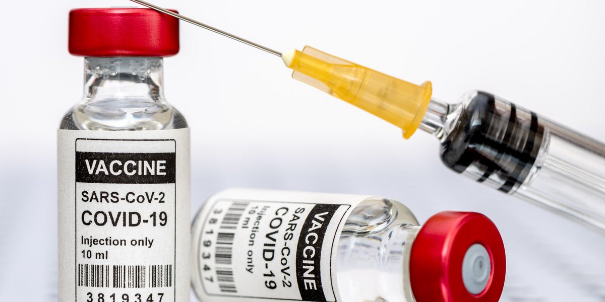 Impfnadel und zwei Fläschchen mit Impfserum, beschriftet "Vaccine: SARS-CoV-2, COVID-19"