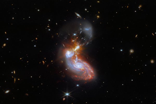 Zwei Galaxien in bläulichem Licht, umgeben von rötlichem Nebel, vor schwarzem Hintergrund mit Sternen