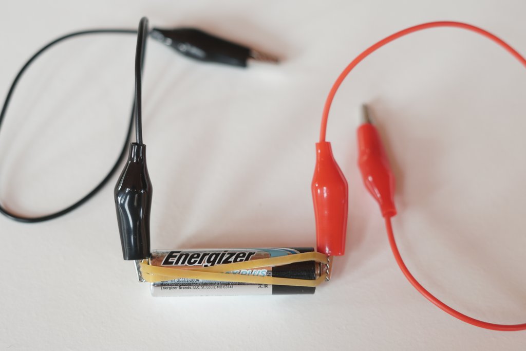 Batterie mit Gummiband und zwei an den Polen festgeklemmten Krokodilklemmen