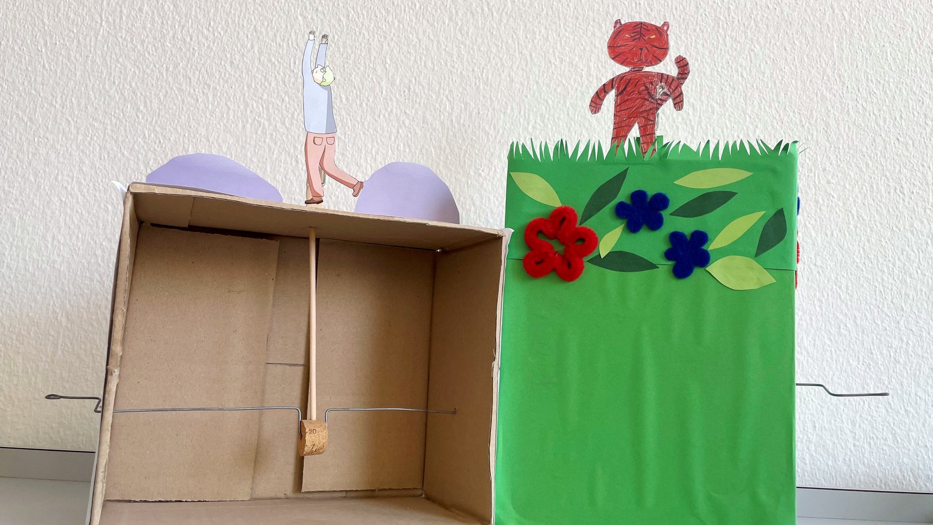 Une boite en carton, un pic en bois, un bouchon de liège, un morceau de fil de fer et un personnage en papier assemblés en un théâtre à manivelle