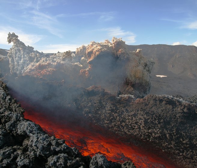Vulkanisches Gebiet unter blauem Himmel, Blick in eine rötlich glühende Erdspalte