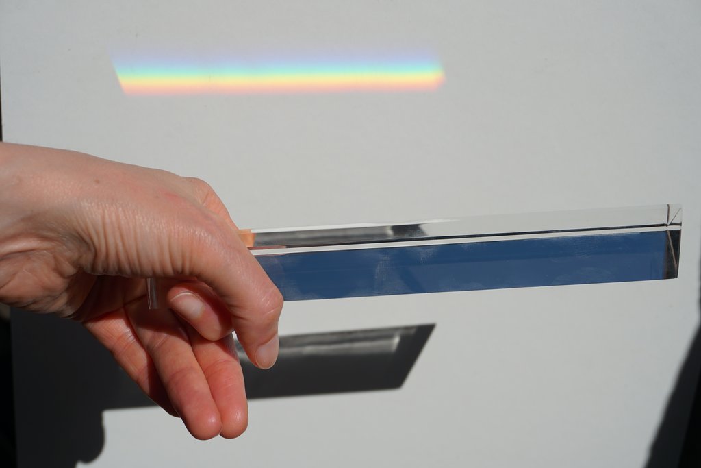 Hand mit Glasprisma und Regenbogenprojektion an der Wand