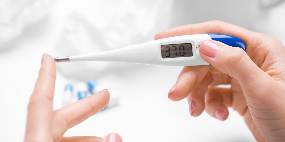 Hände einer Frau zeigen ein digitales Thermometer mit der Temperatur 37°C