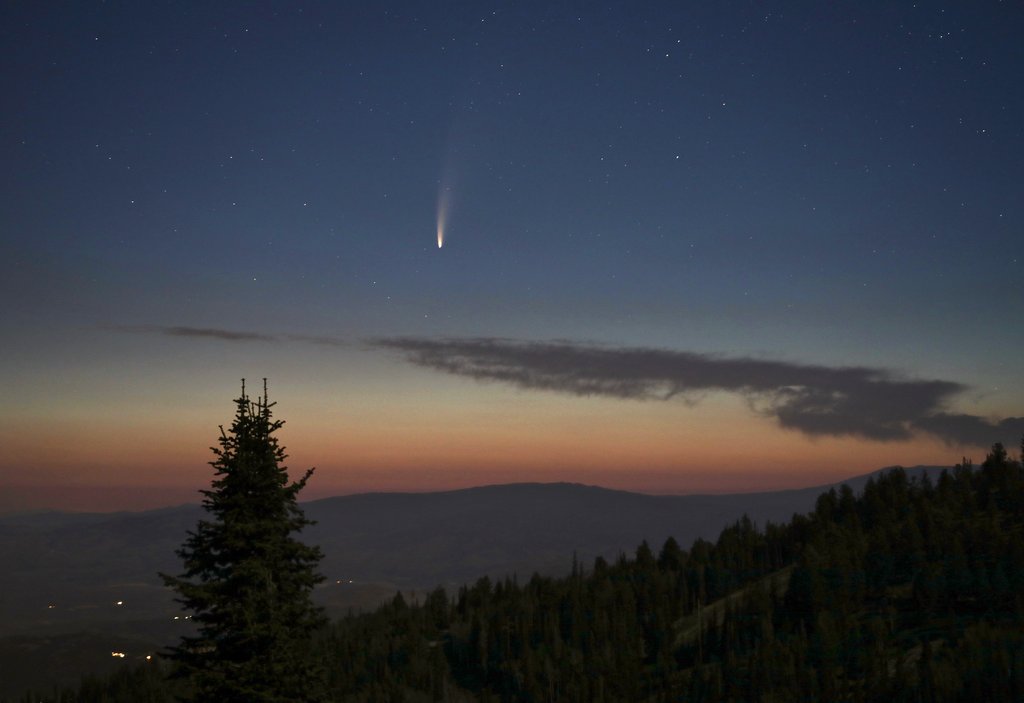 Komet mit senkrecht stehendem Schweif in der Abenddämmerung über einer hügeligen, mit Nadelbäumen bewachsenen Landschaft