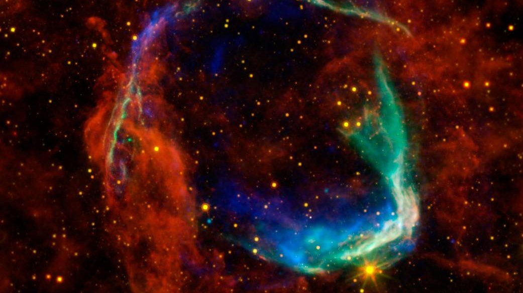 In Rot-, Blau- und Grüntönen eingefärbtes Bild von Staub- und Gasschlieren, wie Teleskope sie bei verschiedenen Wellenlängen erfassen.