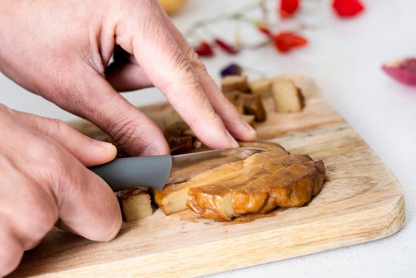 Hände schneiden ein Schnitzel auf Holzbrett