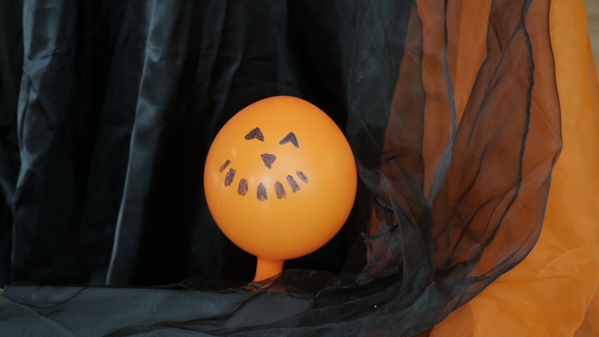 Oranger Luftballon mit aufgemaltem Gesicht, das an einen geschnitzten Kürbis erinnert