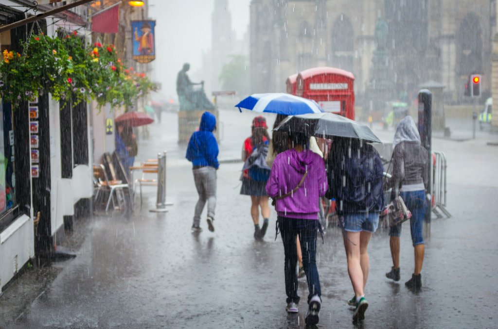 Gruppe von Menschen, die mit Schirmen im heftigen Regen durch eine Strasse gehen.