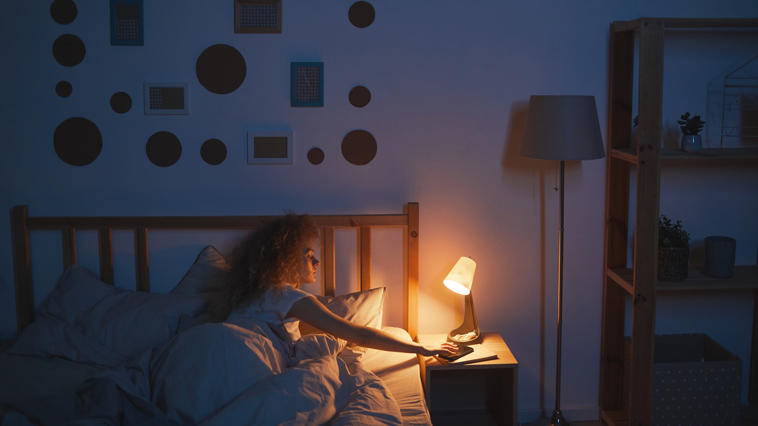 Junge Frau liegt im Bett im dunklen Schlafzimmer, brennende Nachttischlampe
