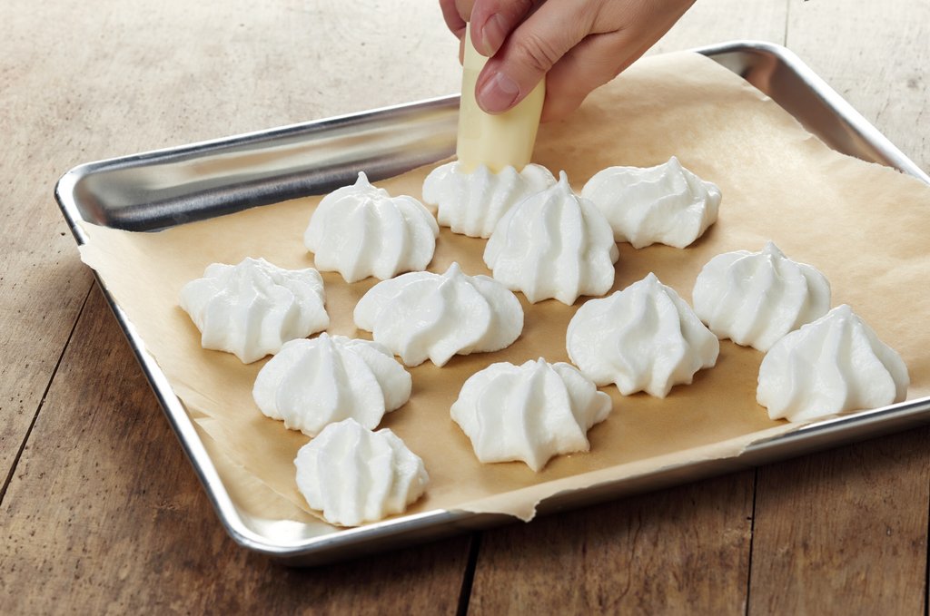 Une main dépose des meringues sur une plaque de cuisson.