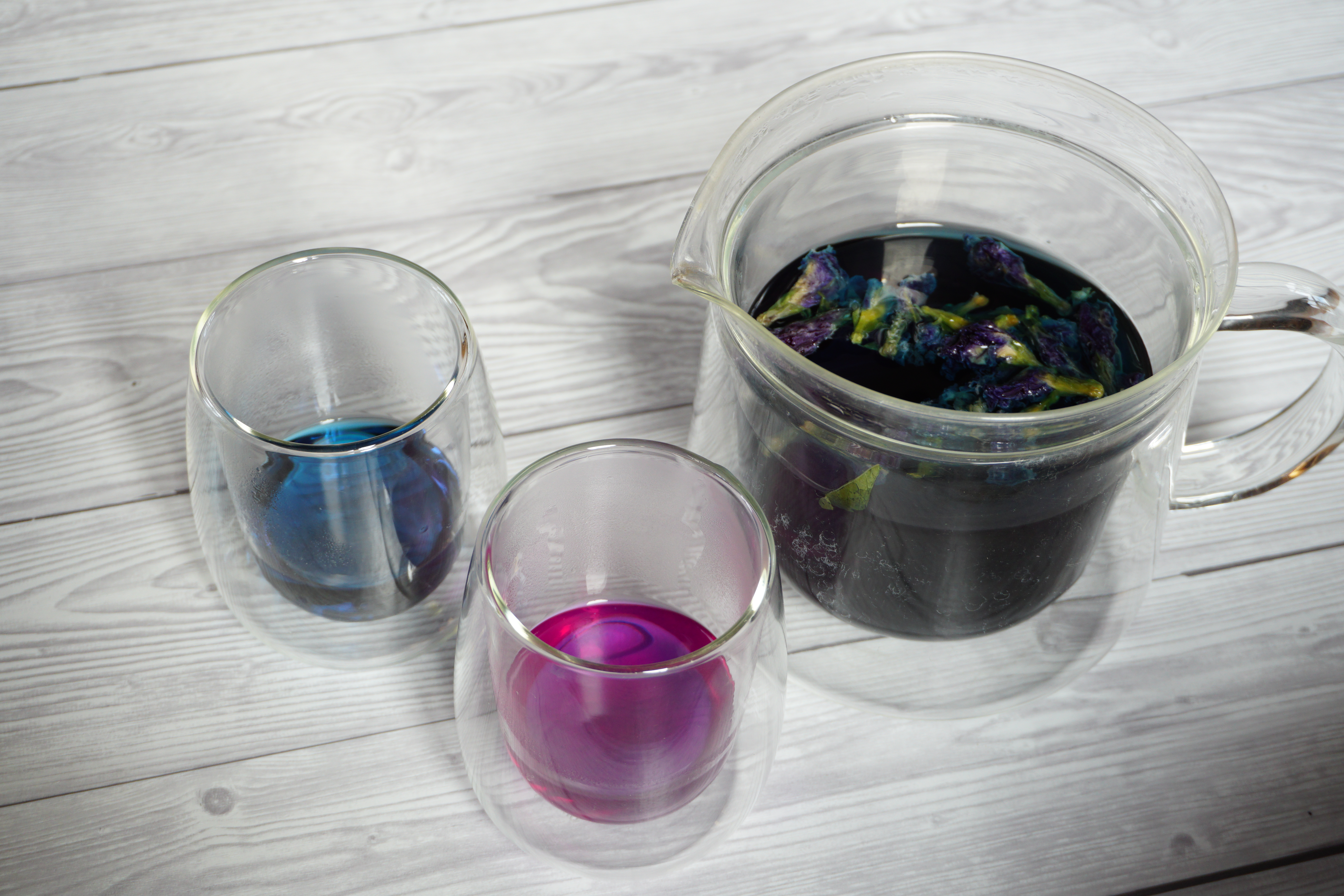 Glaskrug mit blauem Kräutertee; zwei Gläser, davon eines mit blauer, eines mit pinkfarbener Flüssigkeit