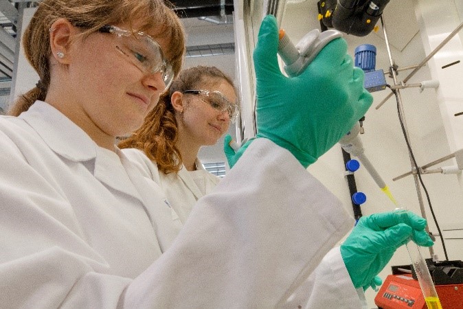 Zwei junge Frauen beim Pipettieren mit Gummihandschuhen im Labor