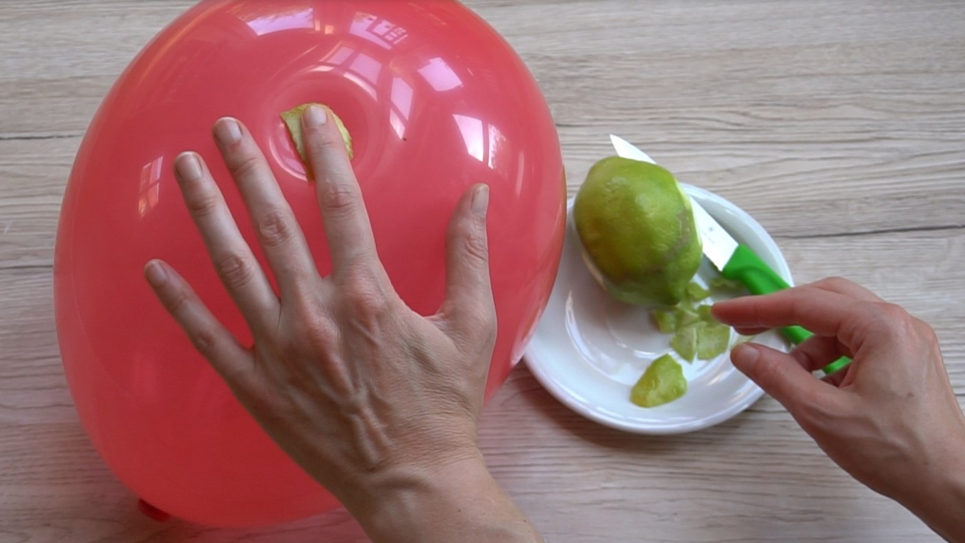 Hand, die auf roten Luftballon drückt, im Hintergrund Zitrone auf Teller