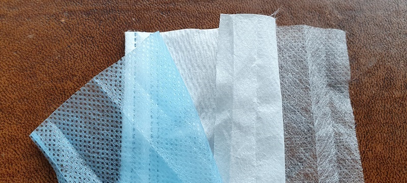 Zerschnittene Hygienemaske, bei der die drei Lagen auseinandergezogen und nebeneinandergelegt wurden